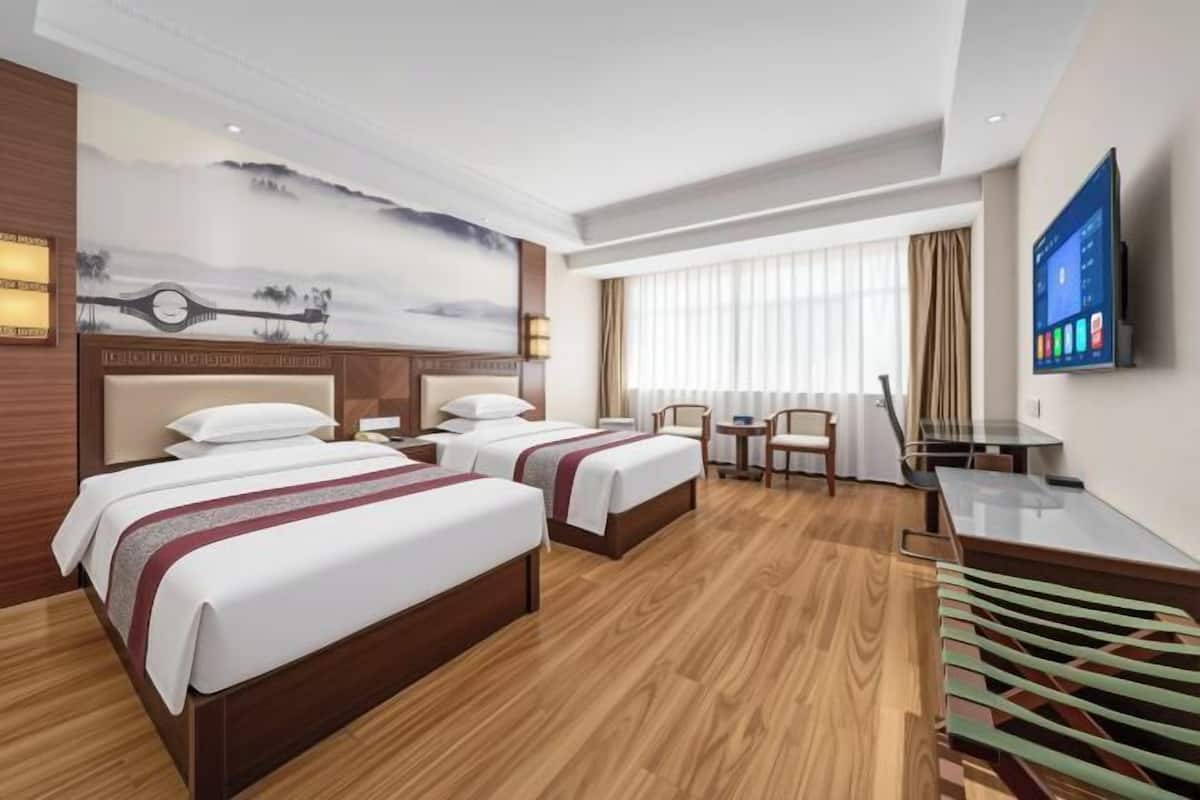 A hotel room with two beds, a desk, a chair, a TV, and a painting on the wall.