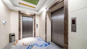 Een lift met een digitaal scherm, een prullenbak en een vloer met een patroon.