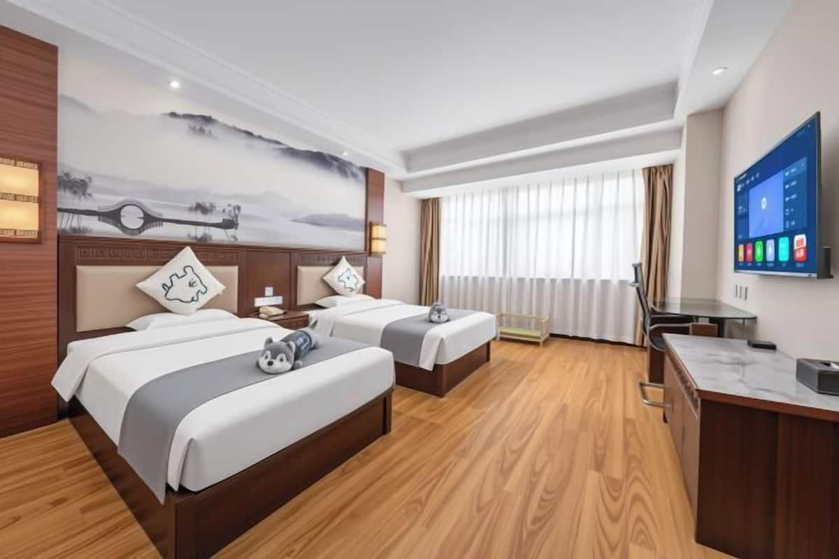 A hotel room with two beds, a desk, a TV, and a painting on the wall.