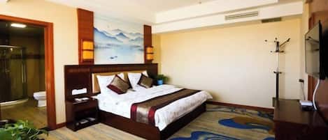 A hotel room with a bed, a shower, a toilet, a TV, and a painting on the wall.