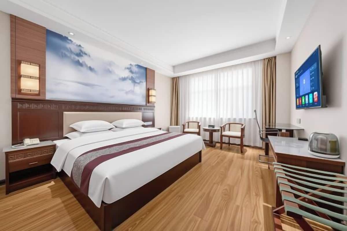 A hotel room with a large bed, a desk, a chair, a television, and a window with curtains.