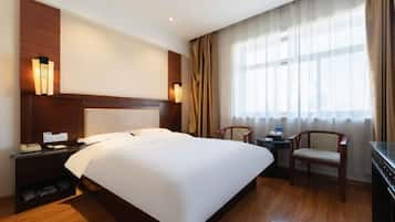 Habitación de hotel con una cama grande, una mesita de noche de madera, un escritorio con silla y un ventanal con cortinas.