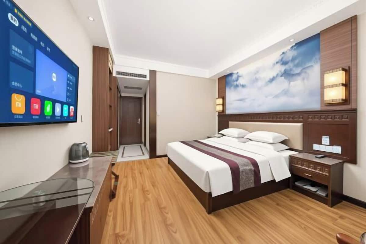 A modern hotel room with a large bed, a desk with a flat-screen TV, a wooden floor, and a wall-mounted artwork.