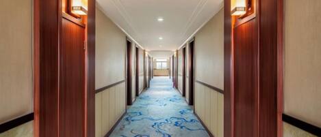 A hotel hallway with wooden doors, a carpet with a blue pattern, and wall sconces.