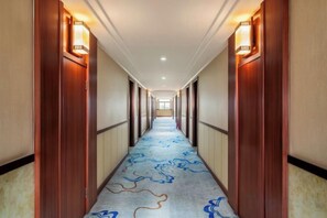 A hotel hallway with wooden doors, a carpet with a blue pattern, and wall sconces. - Sunshine Holiday Hotel (Wuwei)