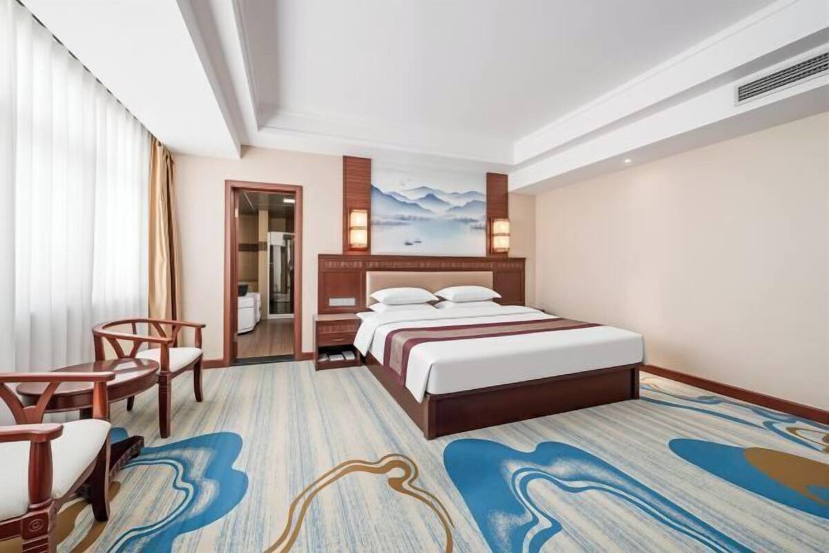 A hotel room with a bed, a desk, a chair, and a painting on the wall.
