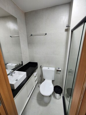 Une salle de bain avec des toilettes blanches, un lavabo et un espace douche.