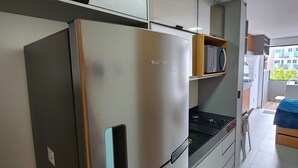 A modern kitchen with a stainless steel refrigerator, a built-in oven, and a countertop with a coffee-themed mat. - Flat Ofurô 02 VP by La Playa (Ipojuca)