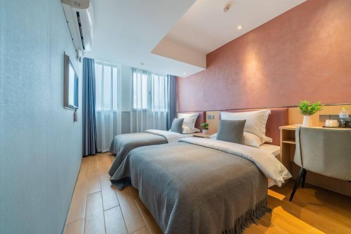 A hotel room with two beds, a desk, a chair, and a small plant.