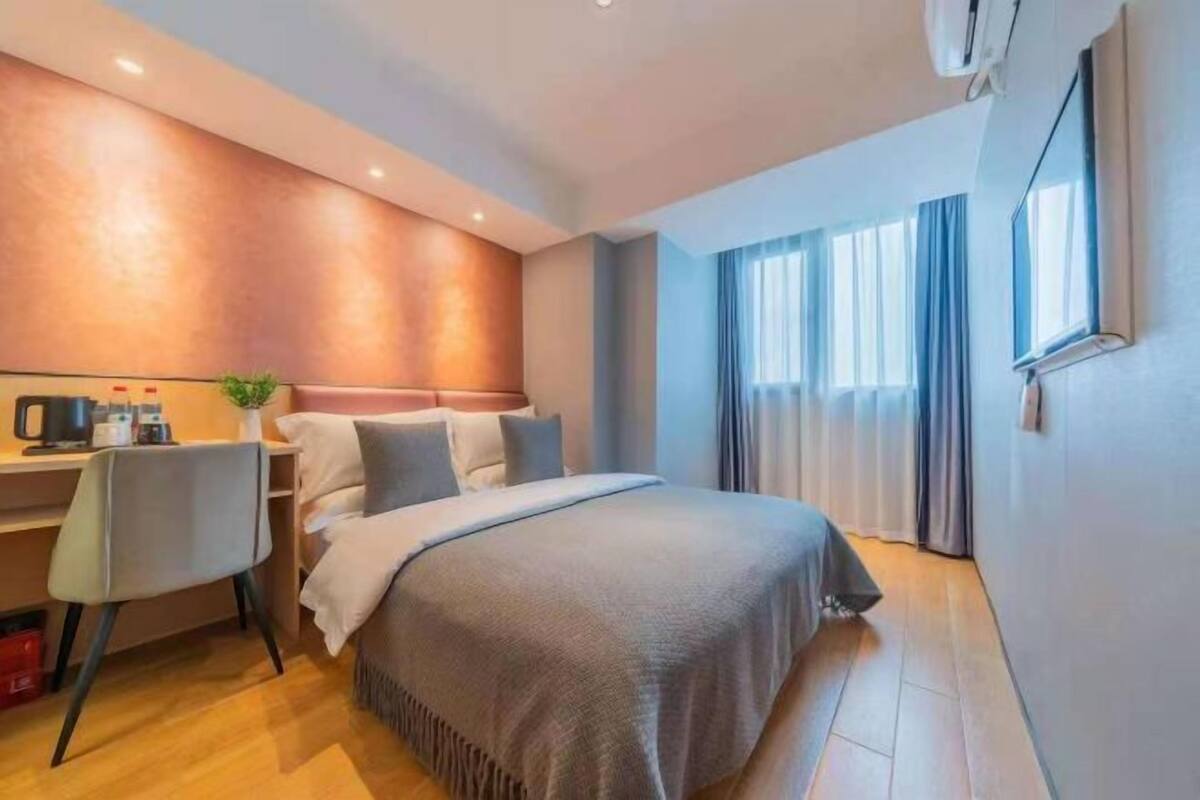 A hotel room with a bed, a desk, a chair, and a window with curtains.