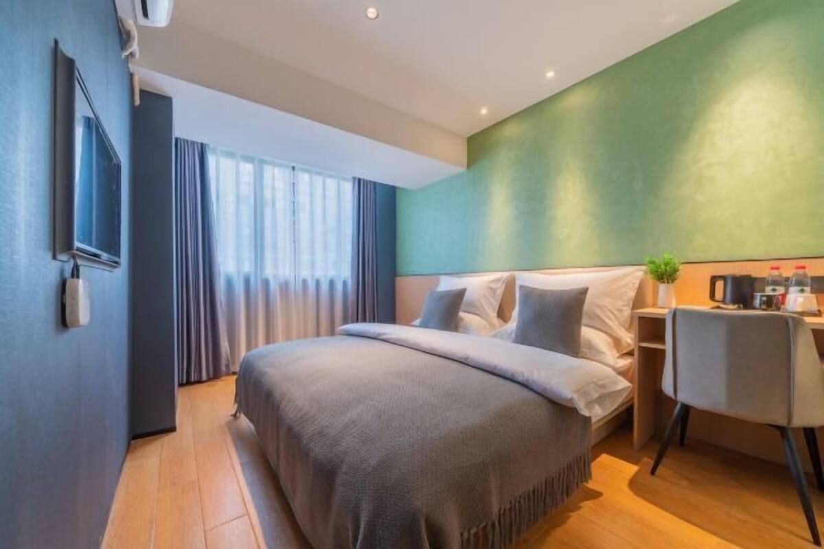 A modern hotel room with a large bed, a desk, and a view of the city.