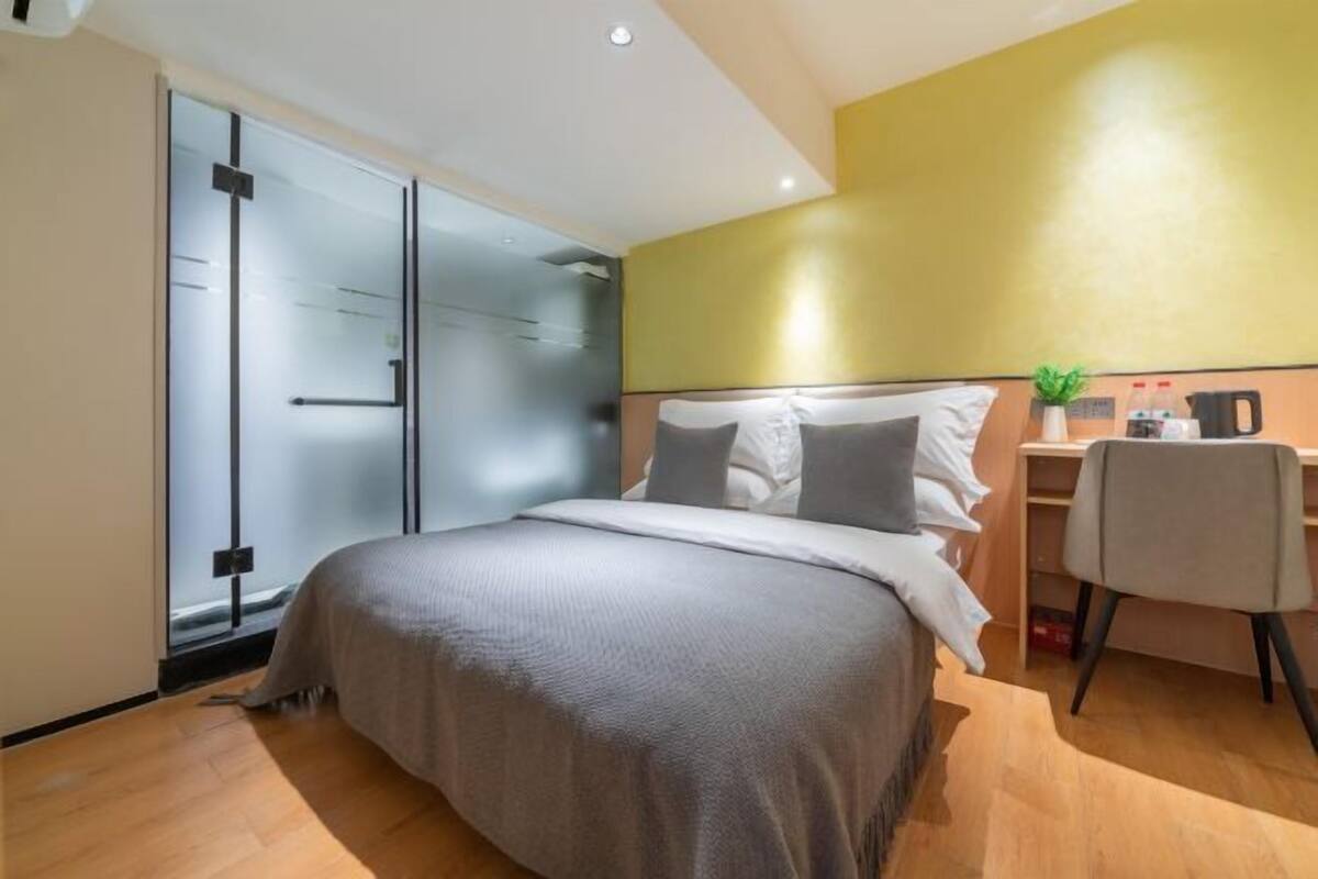 A modern hotel room with a bed, a desk, a chair, and a sliding glass door.