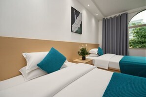 Ett hotellrum med två sängar, ett nattduksbord, en krukväxt och ett fönster med gardiner.