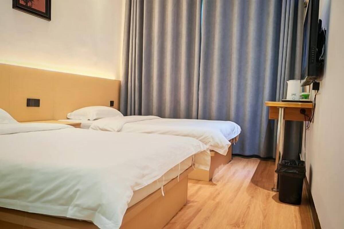 Quarto de hotel com duas camas, piso de madeira, televisão e cortina.