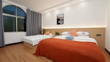 Quarto de hotel com uma cama grande, uma cama menor, uma janela com cortinas, uma obra de arte na parede e uma mesa de cabeceira com abajur.