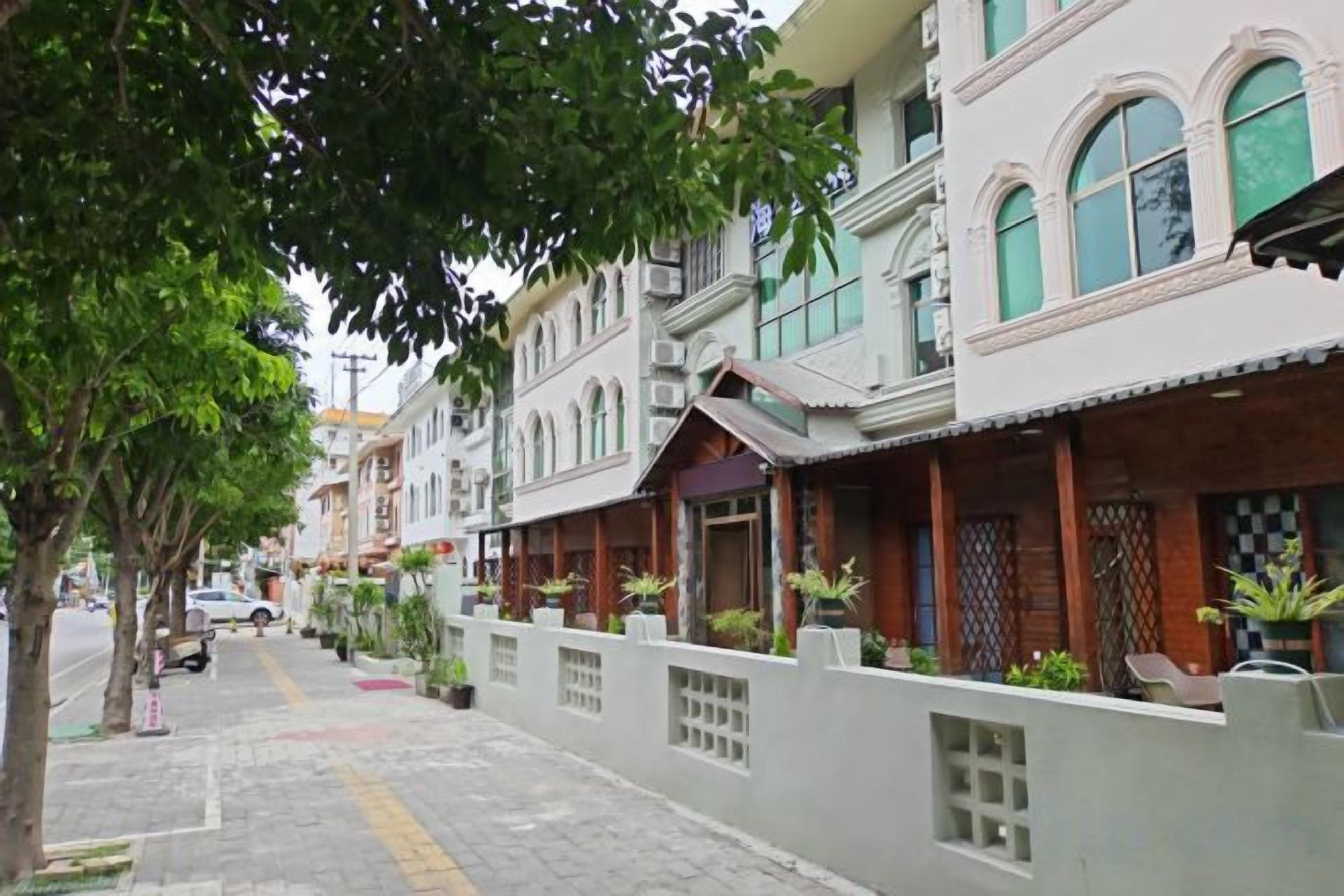 A row of traditional buildings with balconies, a paved sidewalk, and potted plants.
