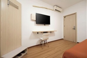 Habitación de hotel con cama, televisor montado en la pared, escritorio con silla y armario.