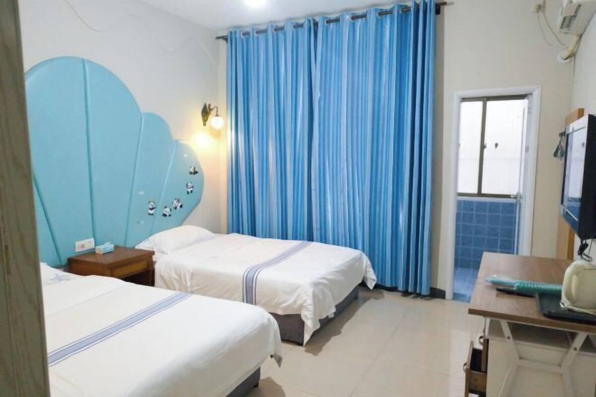 A hotel room with two beds, a desk with a computer, a window with curtains, and a bathroom with a mirror.