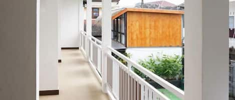 A narrow corridor with white railings, leading to a wooden structure with a sloped roof.