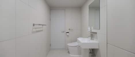 Un baño moderno con azulejos blancos, inodoro, lavamanos y zona de ducha.
