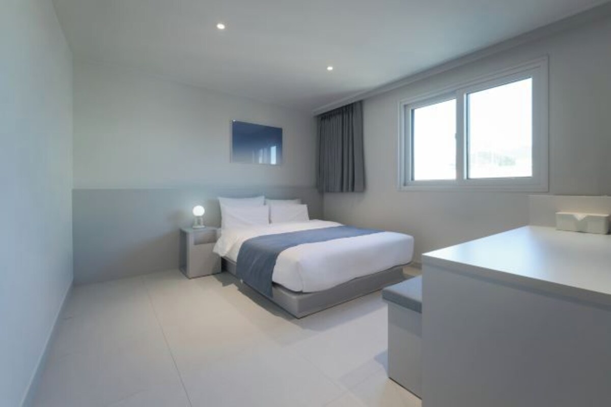 Una habitación de hotel moderna con cama, mesita de noche y zona de escritorio.
