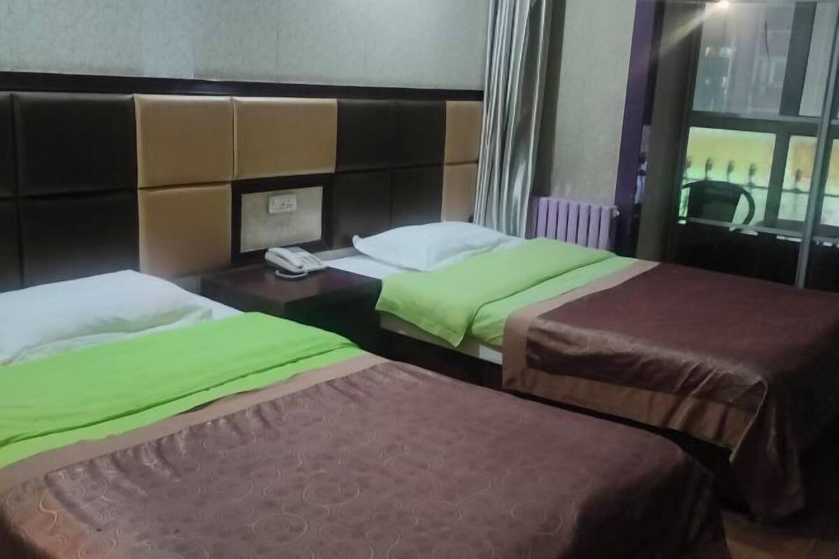 Two single beds with headboards, a bedside table with a phone, and a window with curtains.