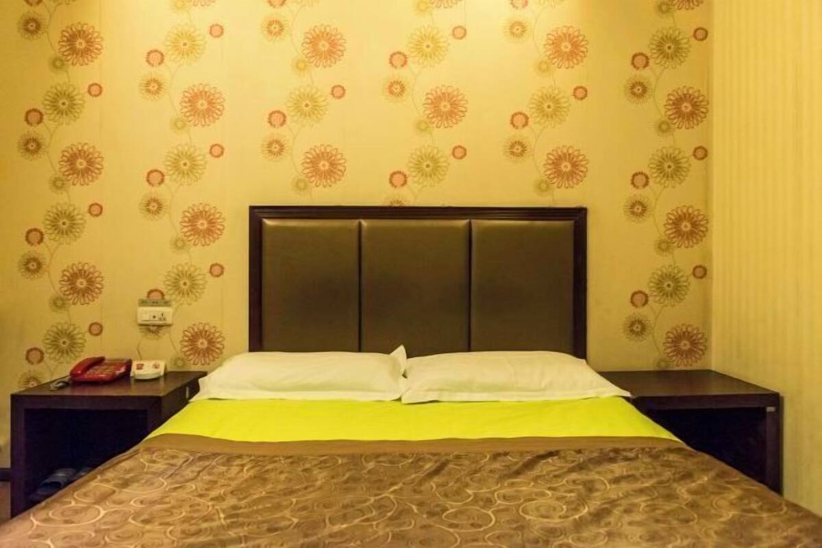 A hotel room with a bed, a nightstand, a telephone, and a wall with a floral pattern.