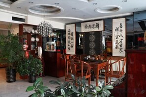 A restaurant interior with a wooden dining table, chairs, potted plants, and a decorative chandelier.