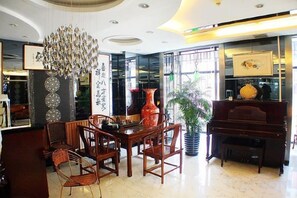 A hotel lobby with a dining area, a piano, and a large vase.