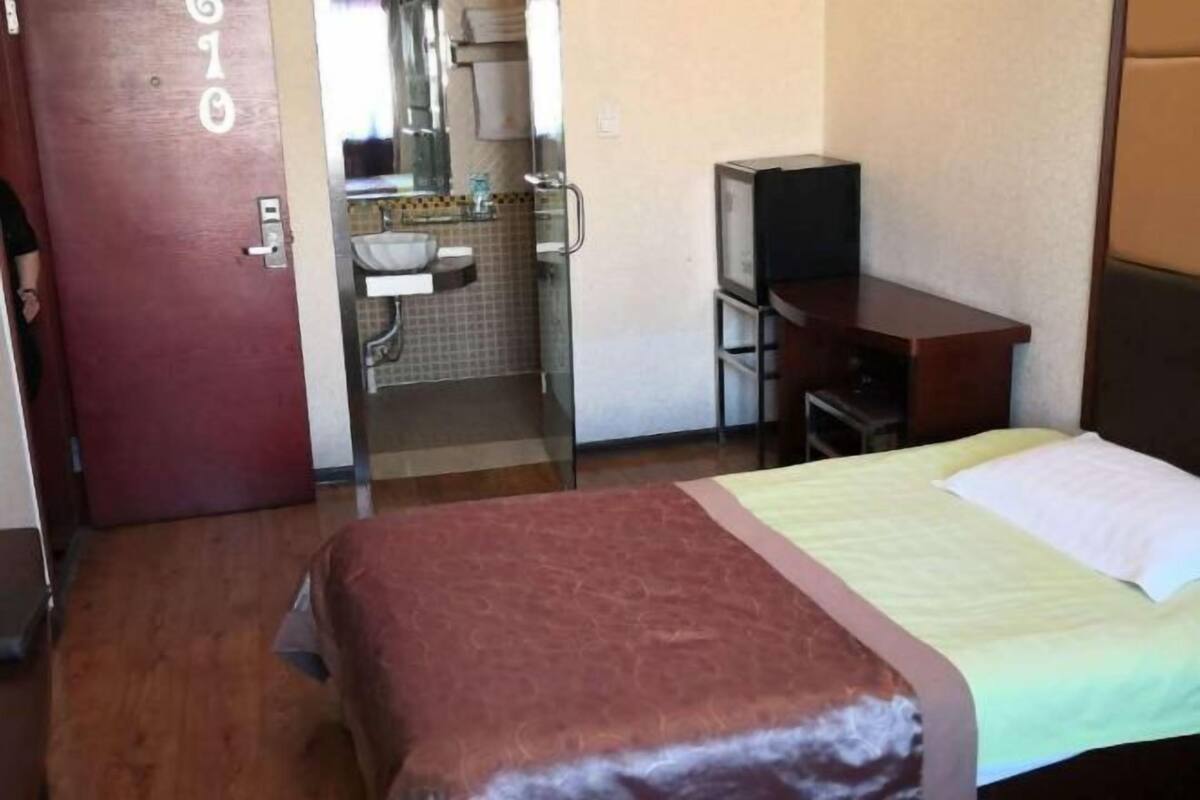 A hotel room with a bed, a television, a desk, and a bathroom visible through an open door.