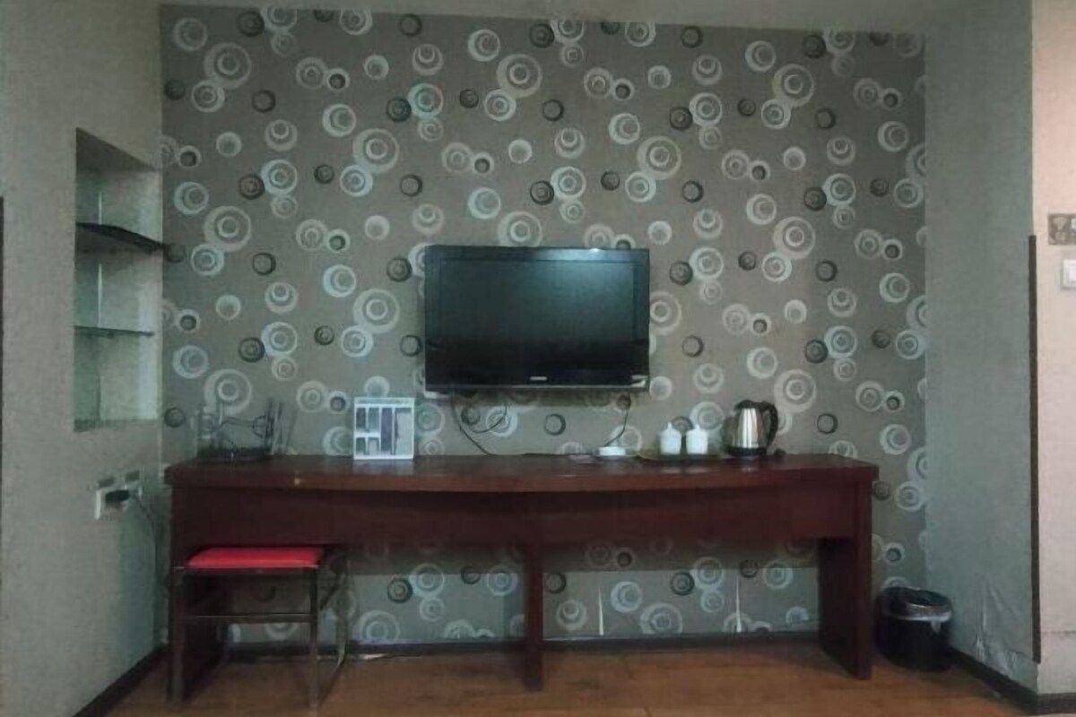 A room with a TV mounted on the wall, a wooden desk with a chair, and a patterned wallpaper.