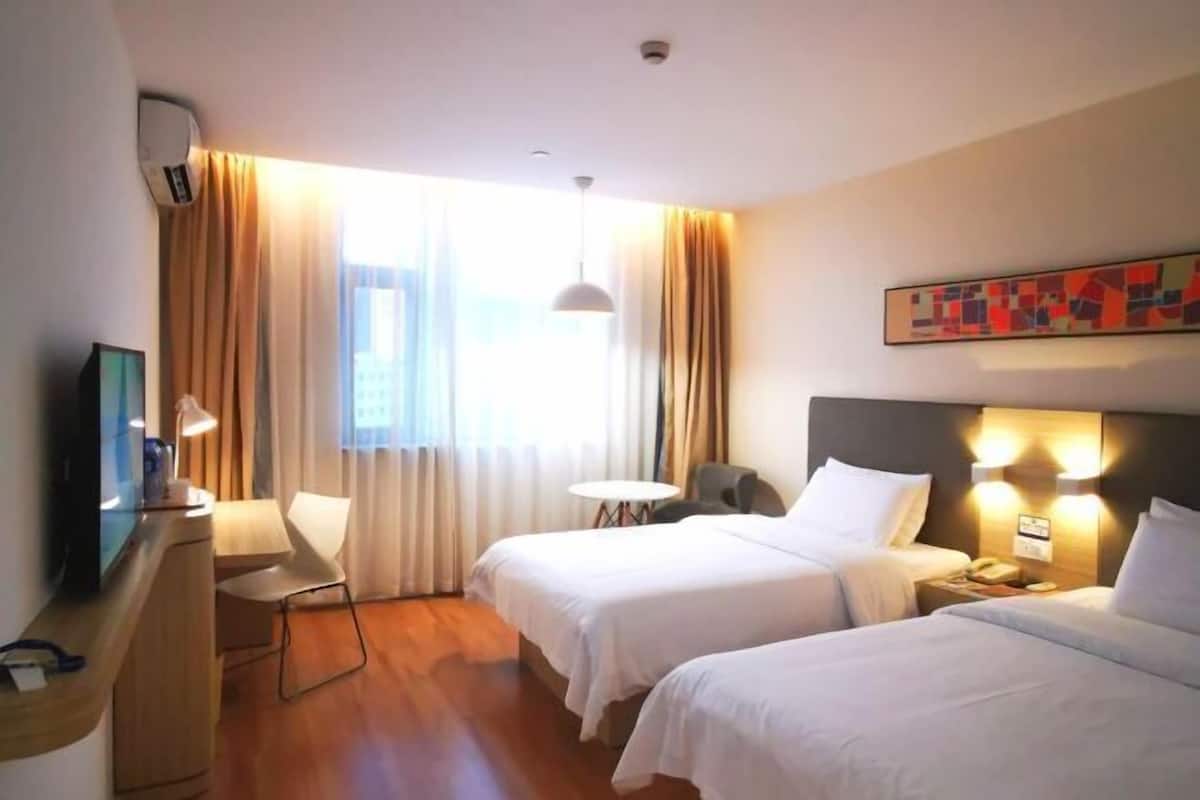 A hotel room with two beds, a desk, a chair, a TV, and a window with curtains.