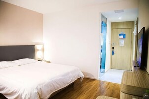Una habitación de hotel con una cama, mesita de noche, lámpara y televisor.
