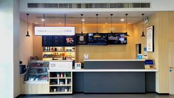 Interior de una cafetería con mostrador, cartel de menú y exhibición de productos de café.