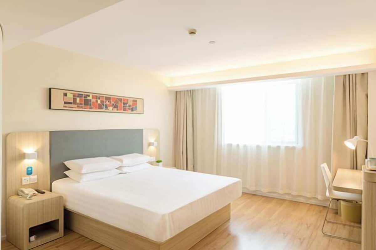A hotel room with a bed, bedside table, lamp, and a painting on the wall.