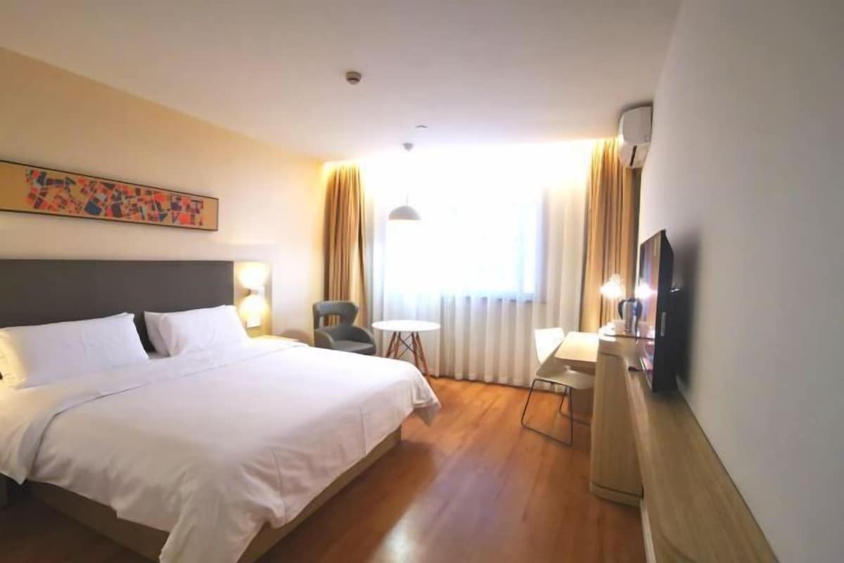 Una habitación de hotel con cama, escritorio, silla, televisor y ventana con cortinas.