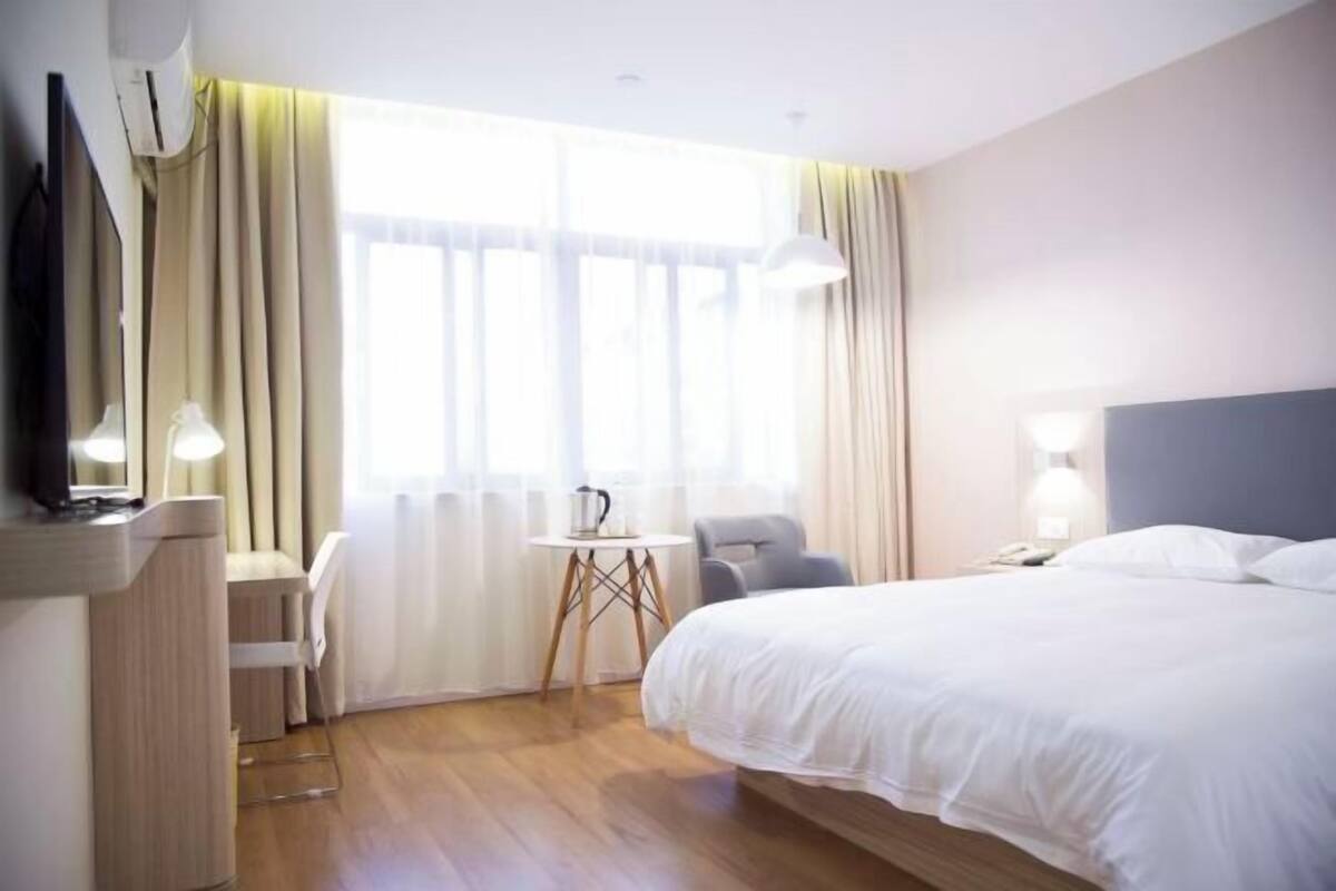 A hotel room with a bed, a desk, a chair, a small table, and a window with curtains.