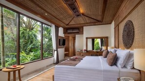 A bedroom with a large bed, a TV, a mirror, and a view of greenery. - Sakti Garden Resort & Spa (Ubud)
