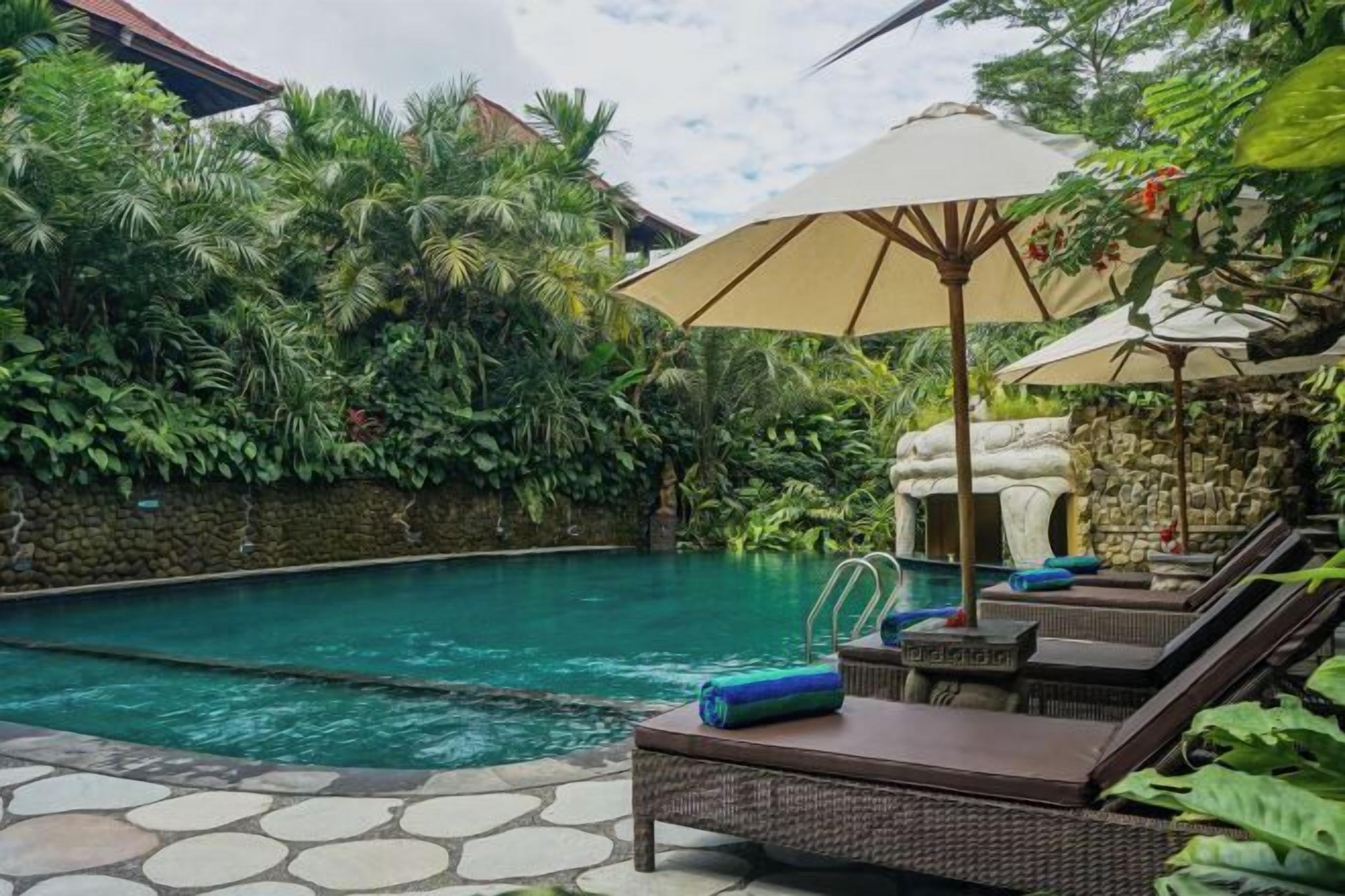 A pool area with lounge chairs, a stone pathway, and lush greenery.