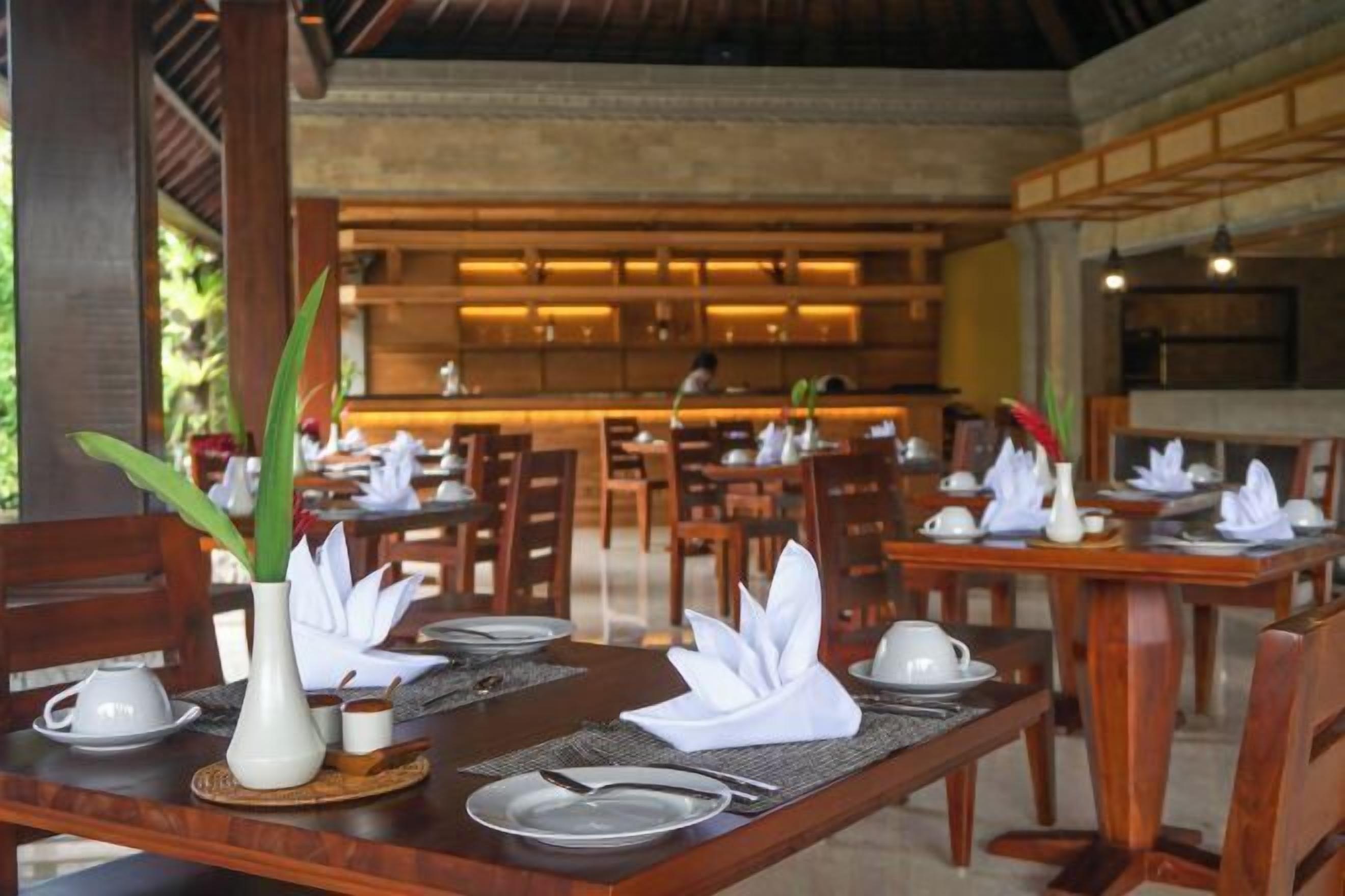 Un restaurante con mesas y sillas de madera, cada conjunto con platos, cubiertos y servilletas.