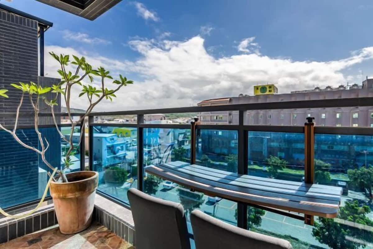 A balcony with a view of a cityscape, a potted plant, and a wooden bench.