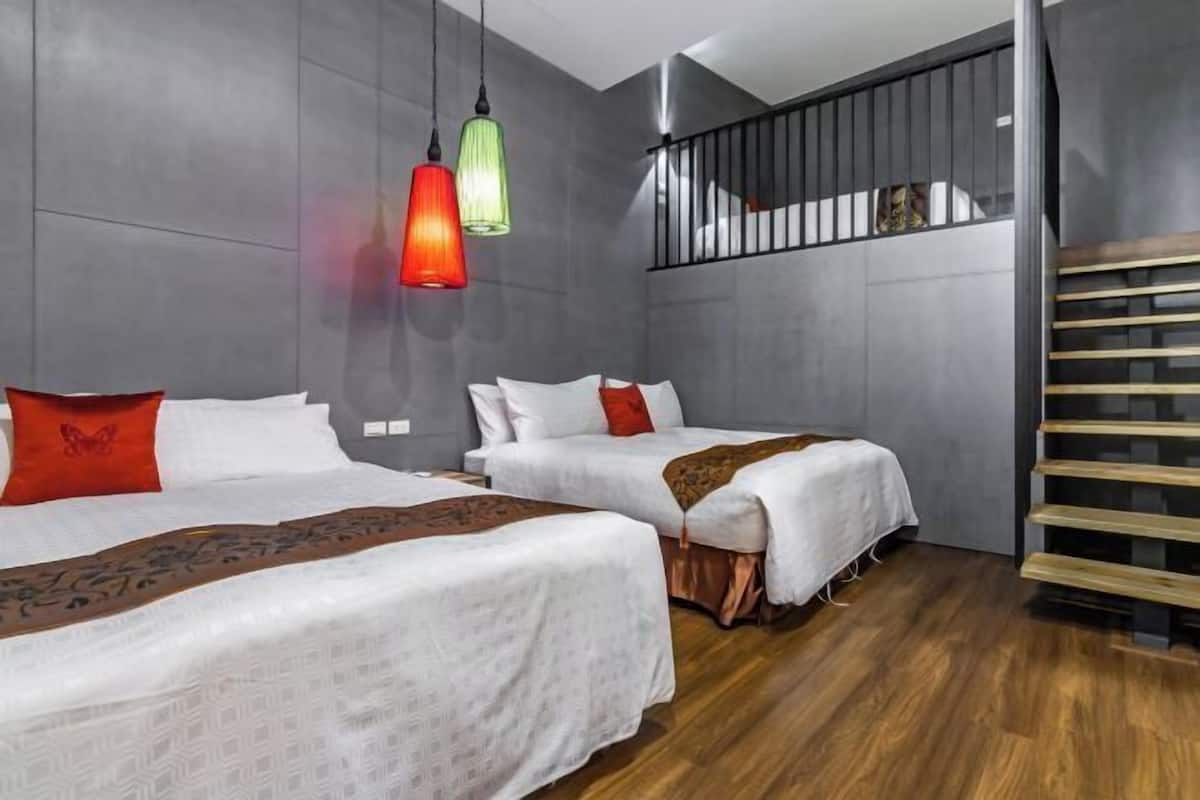 A modern hotel room with two beds, grey walls, wooden flooring, and a balcony with a metal railing.