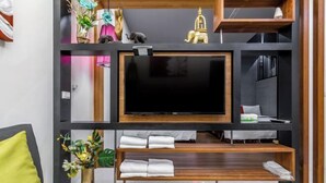 Ein modernes Wohnzimmer mit Flachbildfernseher, Holzregalen und einem Sofa mit gelbem Kissen.