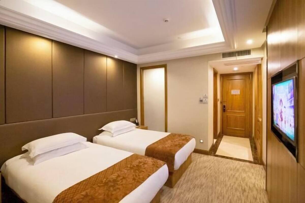 Ein Hotelzimmer mit zwei Betten, einem Fernseher und einer Holztür.