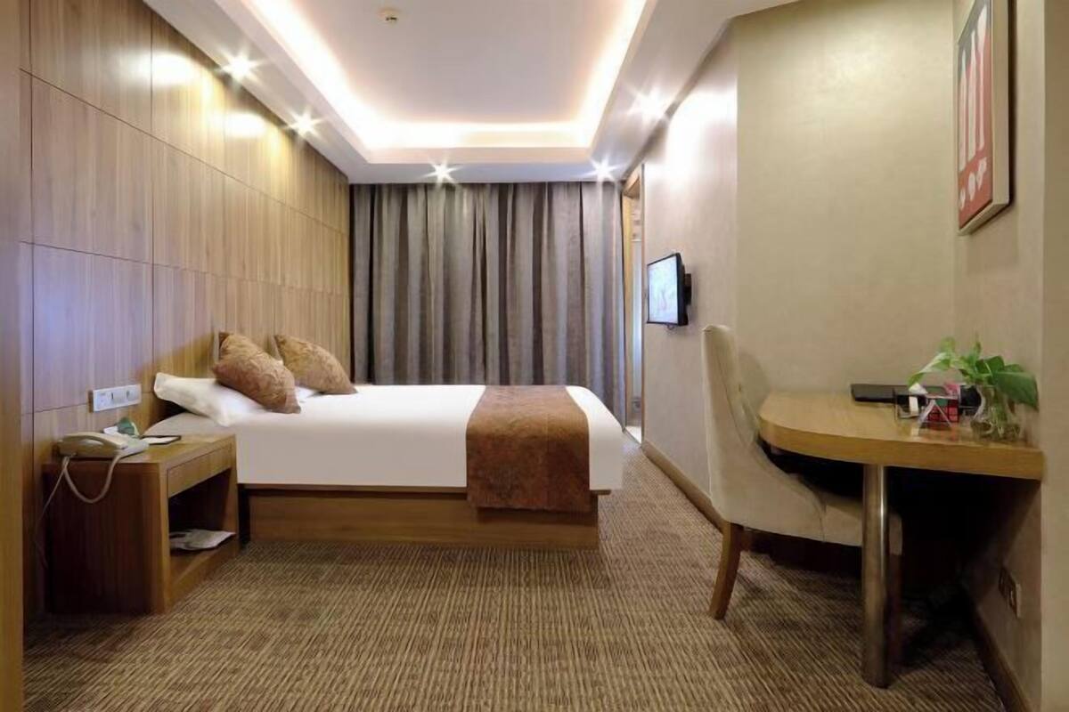Ein Hotelzimmer mit Bett, Nachttisch, Fernseher und einem kleinen Schreibtisch mit Stuhl.