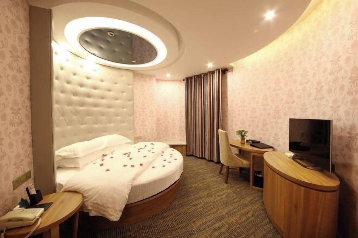 Ein Hotelzimmer mit einem runden Bett, einem Schreibtisch mit Stuhl, einem Fernseher und einem kleinen Tisch mit Telefon.