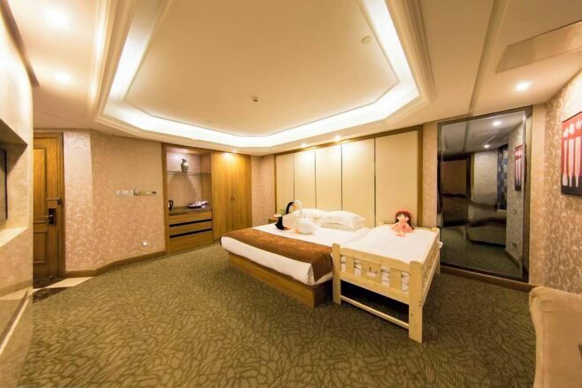 Ein Hotelzimmer mit einem großen Bett, einem Nachttisch aus Holz, einem kleinen Tisch mit Lampe und einem Spiegel an der Wand.