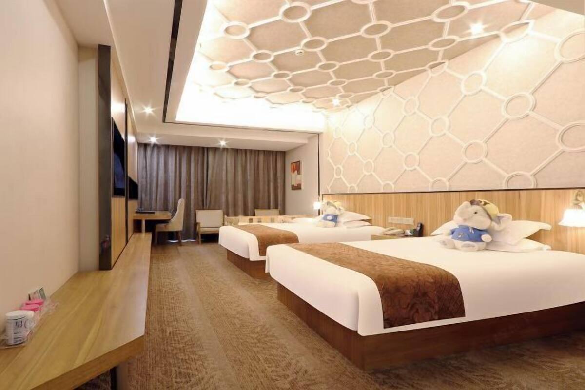 Ein Hotelzimmer mit zwei Betten, einem Schreibtisch, einem Stuhl und einem großen Fenster mit Vorhängen.