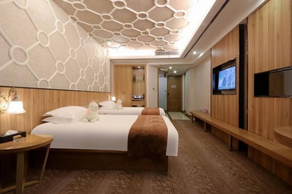 Ein Hotelzimmer mit einem großen Bett, einem Fernseher, einer Holzbank und einem Schreibtisch mit Lampe.