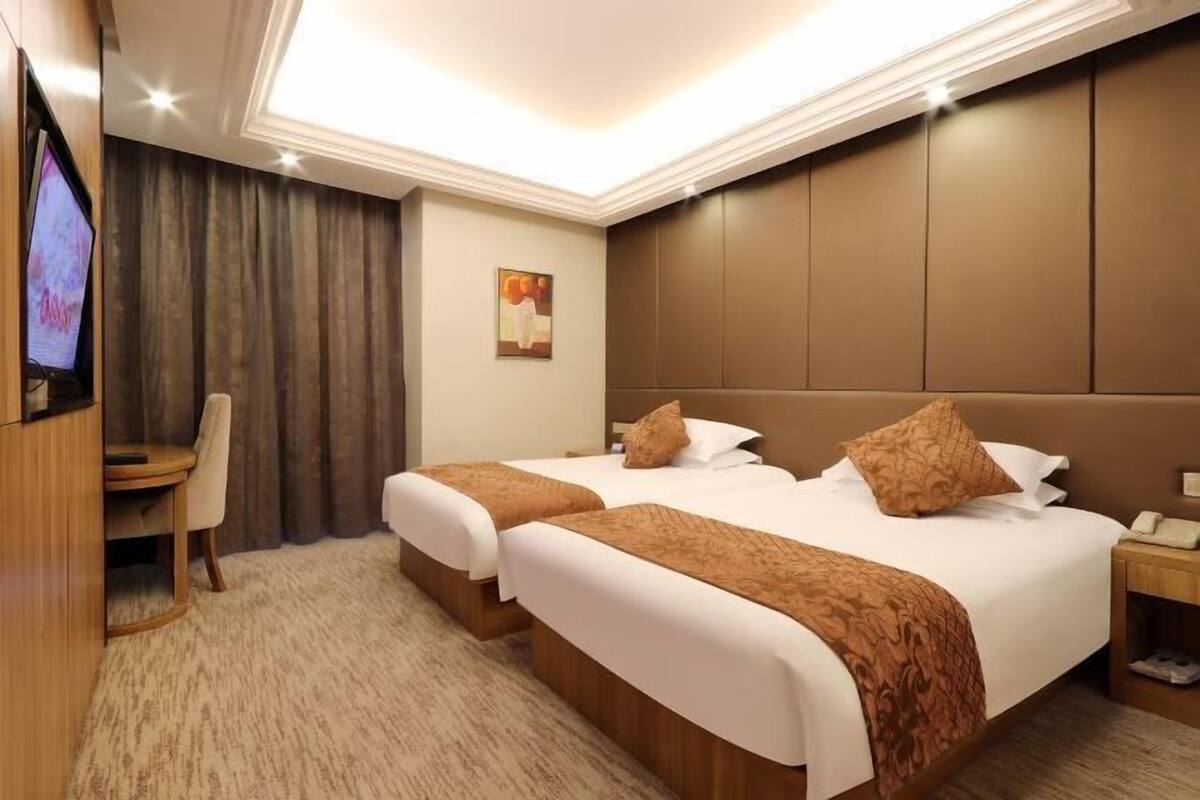 Ein Hotelzimmer mit zwei Betten, einem Fernseher, einem Schreibtisch und einem Bild an der Wand.